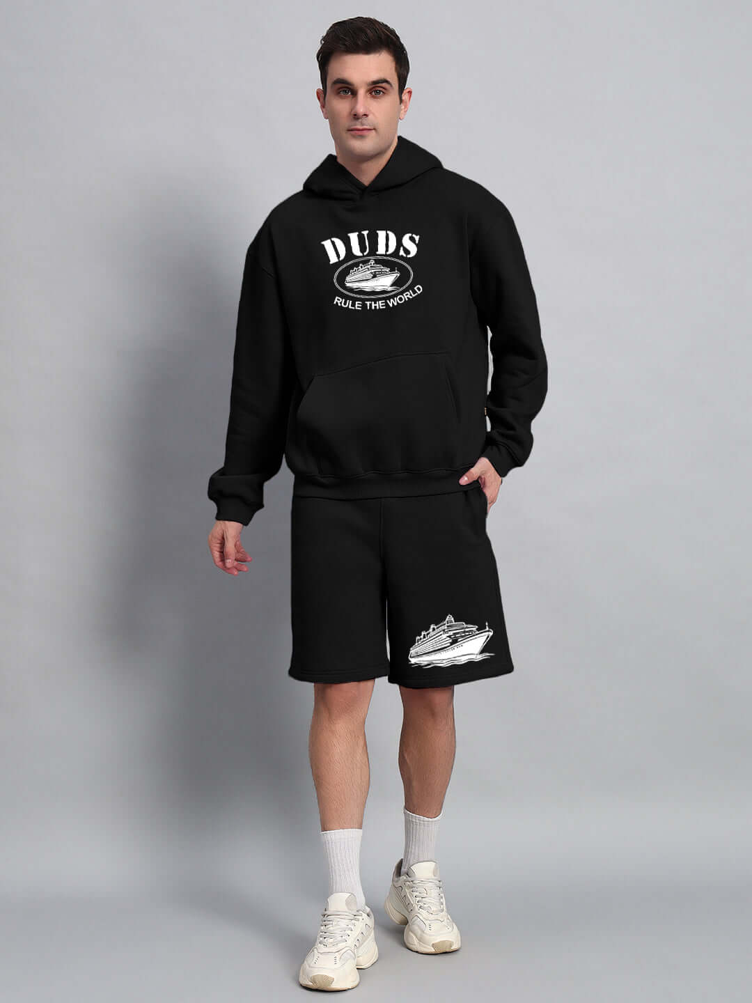Man wearing black 'Rule the World' fleece co-ord by DUDS, standing against gray background. Comfortable and customizable outfit.