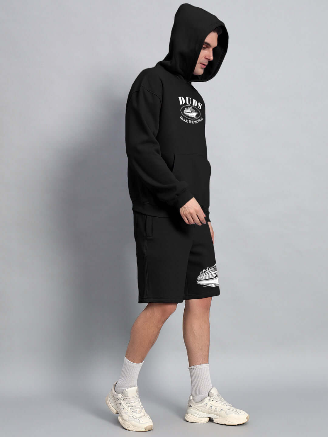 Model wearing black Rule the World Fleece Co-Ord by DUDS, showcasing comfortable hooded sweatshirt and shorts combination.