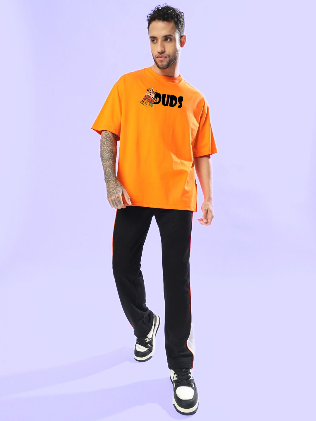 Man wearing SAFARI PRINTED OVERSIZED T-SHIRT ORANGE in a casual style against a light purple background.