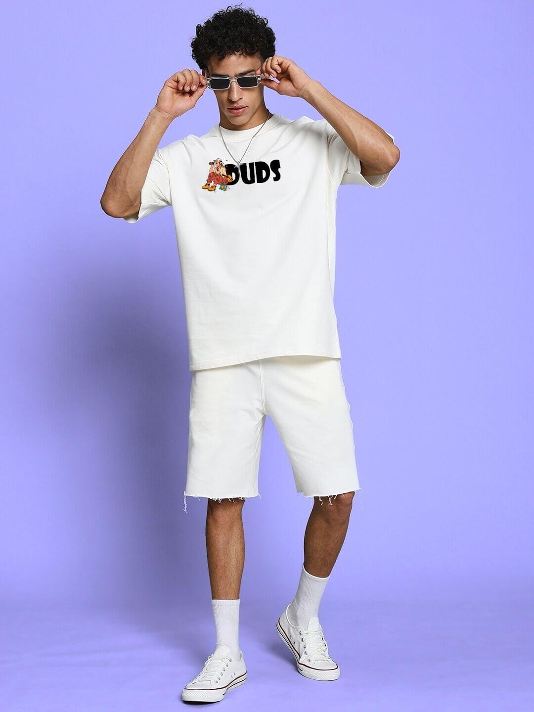Model wearing SAFARI PRINTED OVERSIZED T-SHIRT OFF-WHITE with safari-themed graphic, styled with white shorts and sneakers against a purple backdrop.