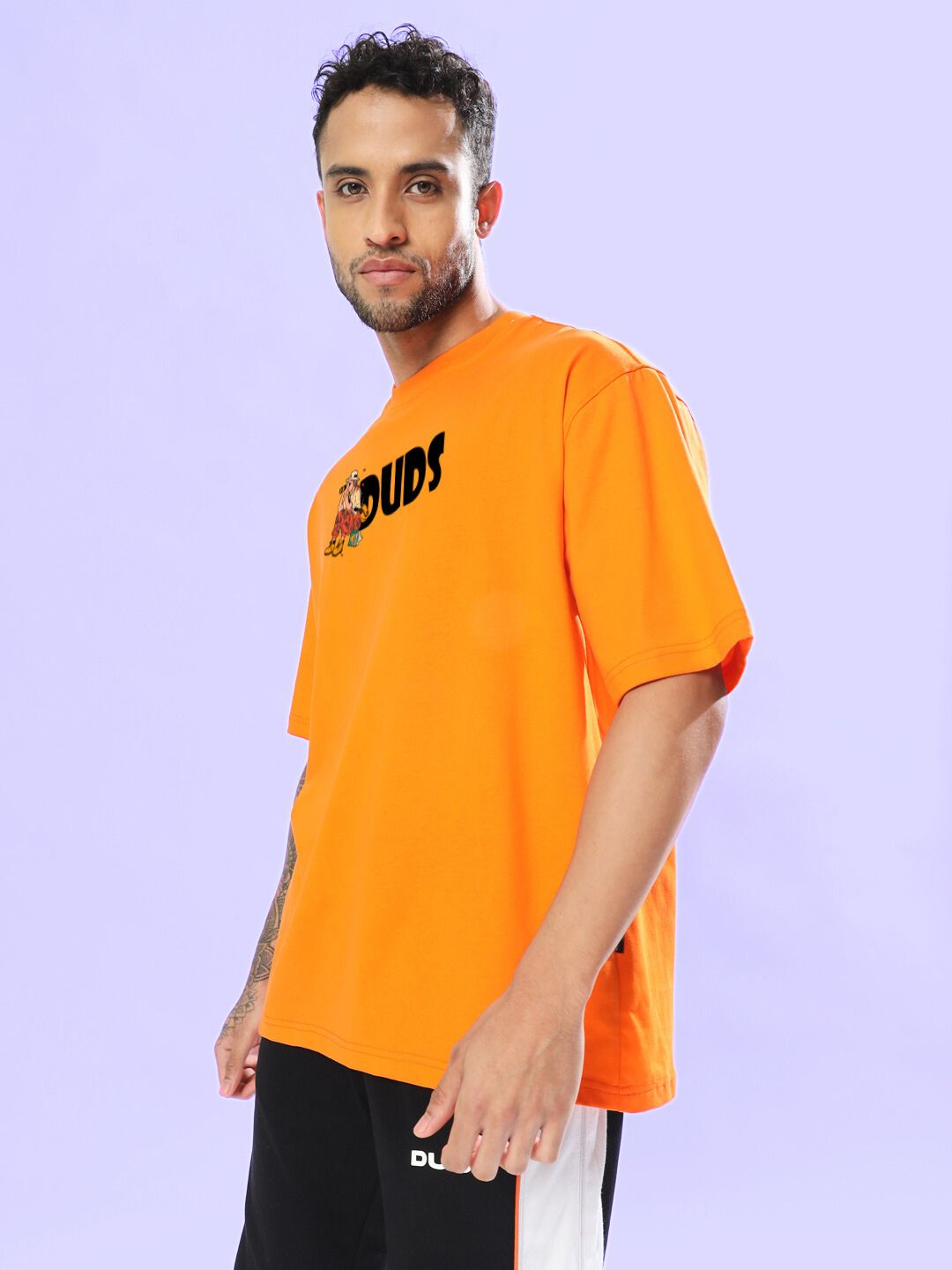 Man wearing SAFARI PRINTED OVERSIZED T-SHIRT ORANGE with black text on front, standing against a purple background.