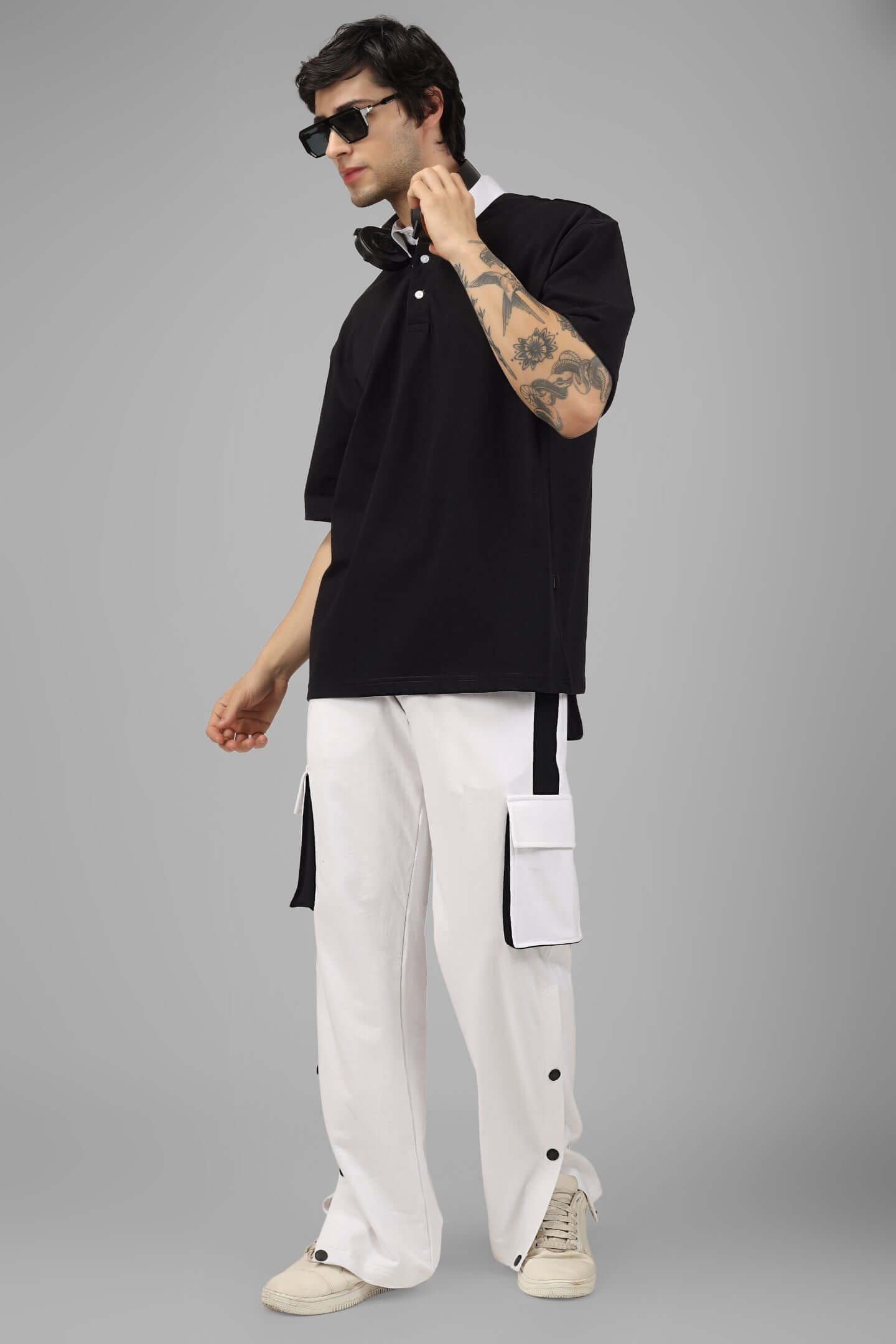 Model in a black oversized polo t-shirt, half sleeves, paired with white cargo pants, showcasing casual streetwear fashion.