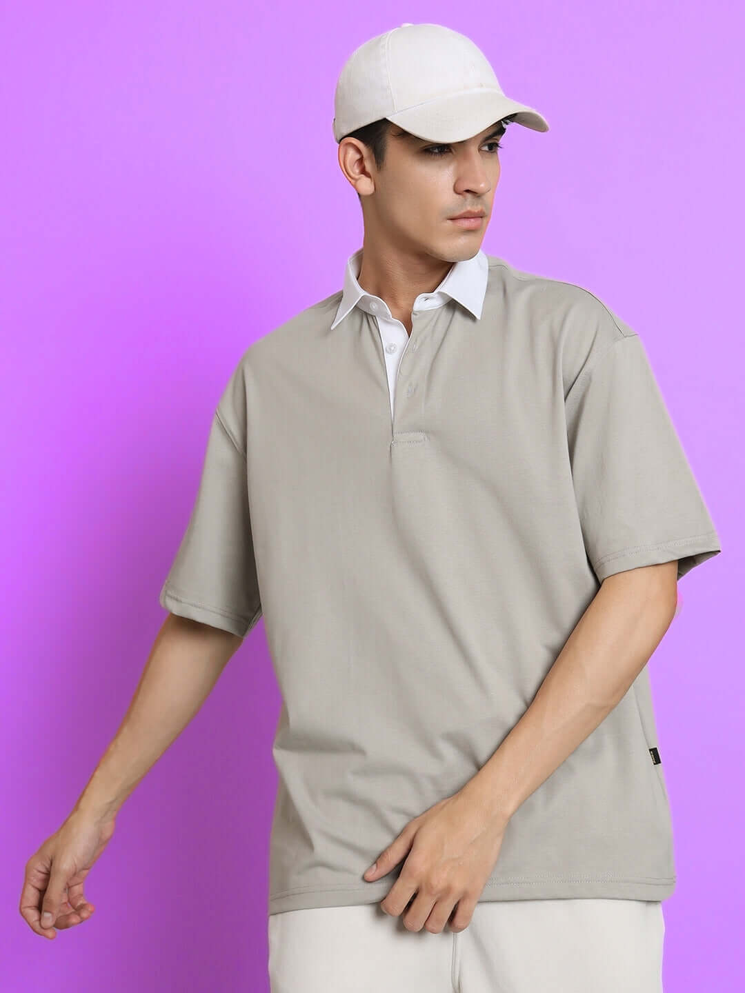 Man wearing SAGOL Polo Oversized T-Shirt in grained grey with short sleeves, showcasing casual fashion on a purple background.