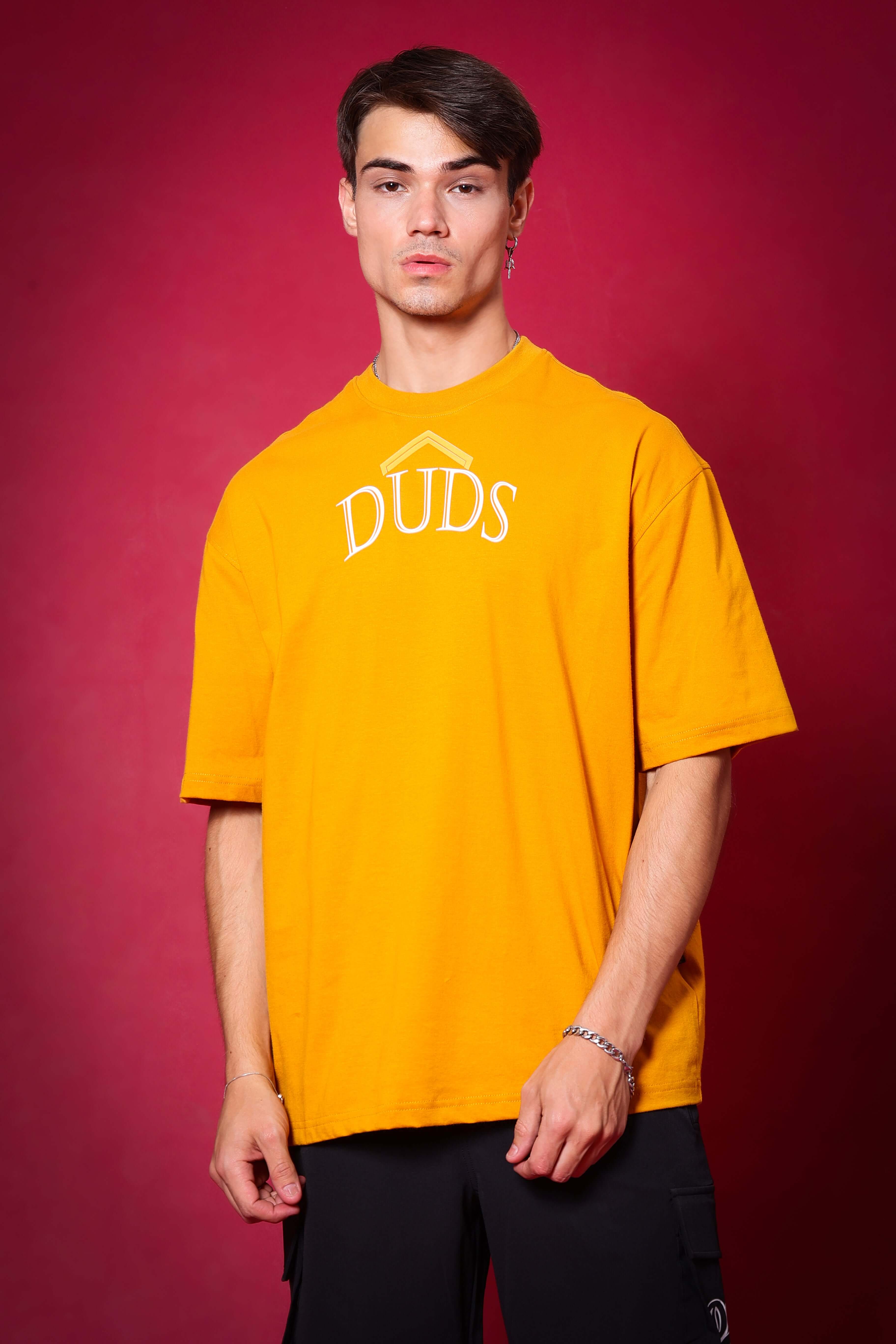 Man wearing mustard SAKURA BLOSSOM over-sized T-shirt with DUDS logo on a red background.