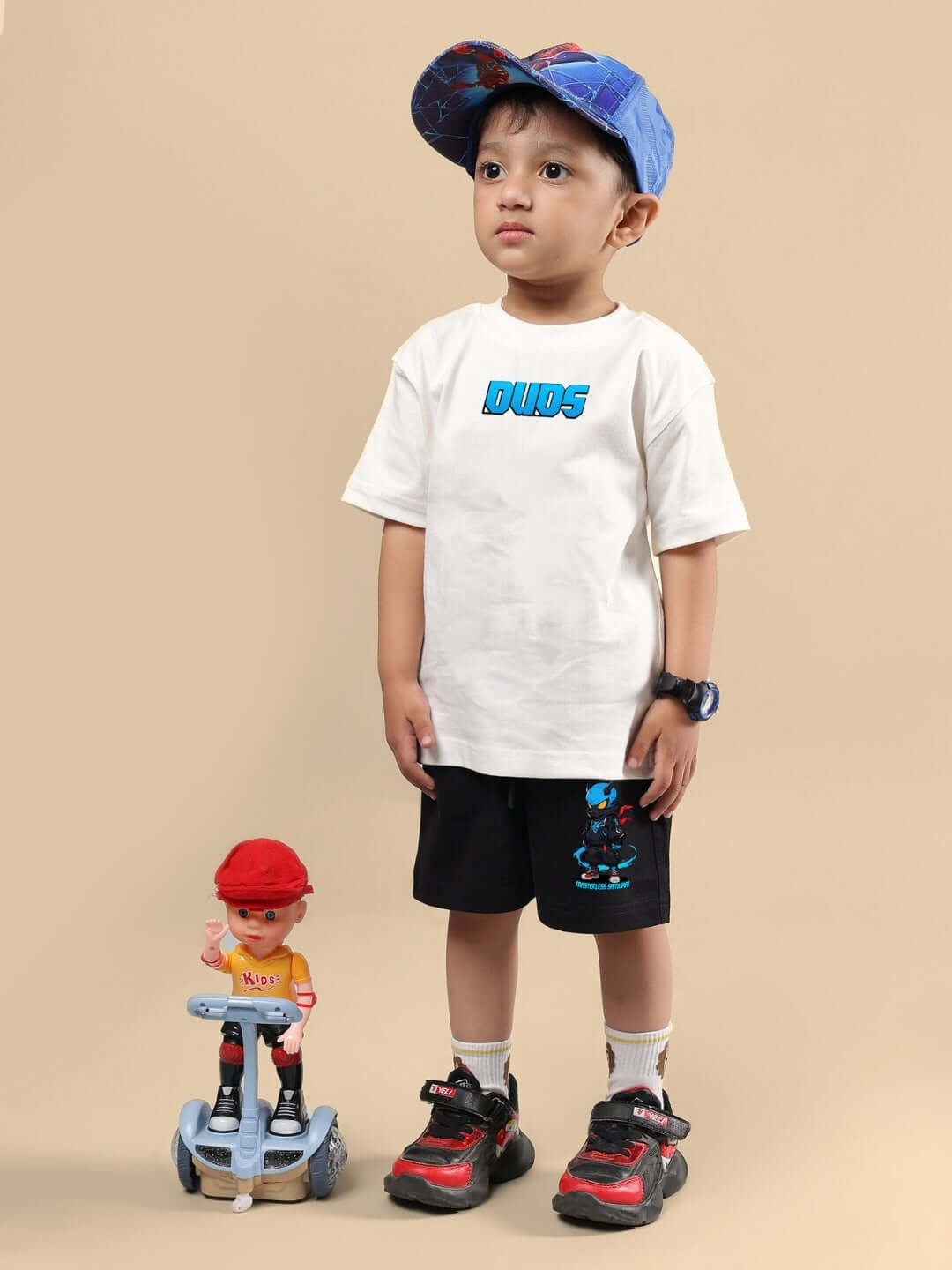 Child wearing Samurai printed co-ord set in off white and black with a cap, standing next to a toy on a beige background.
