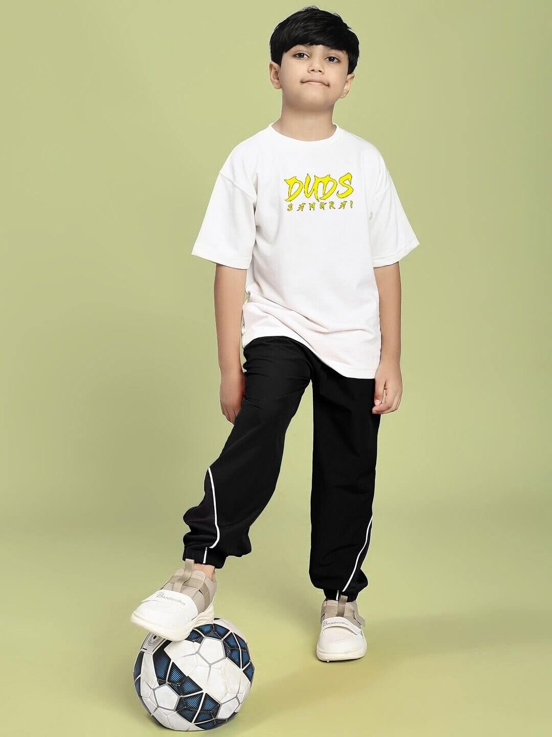 Boy wearing SAMURAI SOUL PRINTED CO-ORD FOR BOYS AND GIRLS WHITE BLACK, standing with a soccer ball on green background.