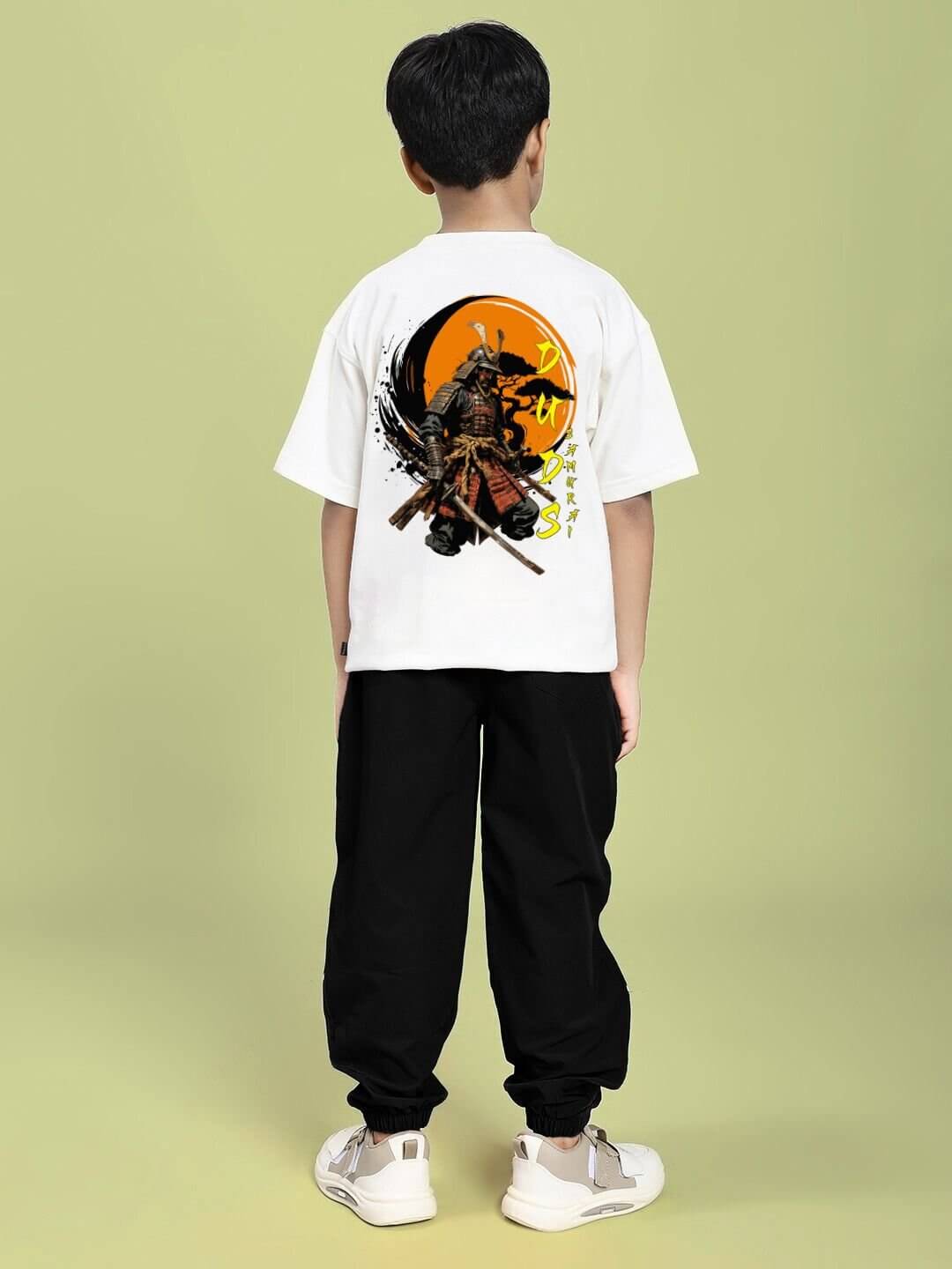 Child wearing SAMURAI SOUL PRINTED CO-ORD FOR BOYS AND GIRLS WHITE BLACK, featuring a samurai design on the back with black pants, standing indoors.