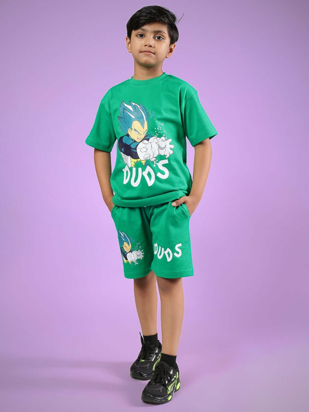 Child wearing green Satoru co-ord set by DUDS, featuring vibrant design, hands in pockets, on a purple background.