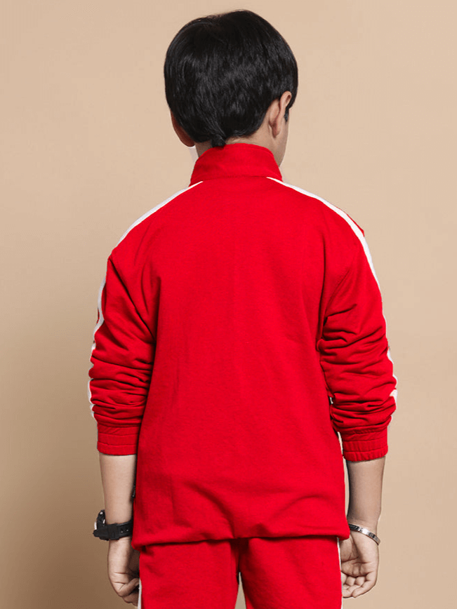 Child wearing red Scotia jacket for boys and girls, featuring white accents, standing against beige background, showcasing back view.