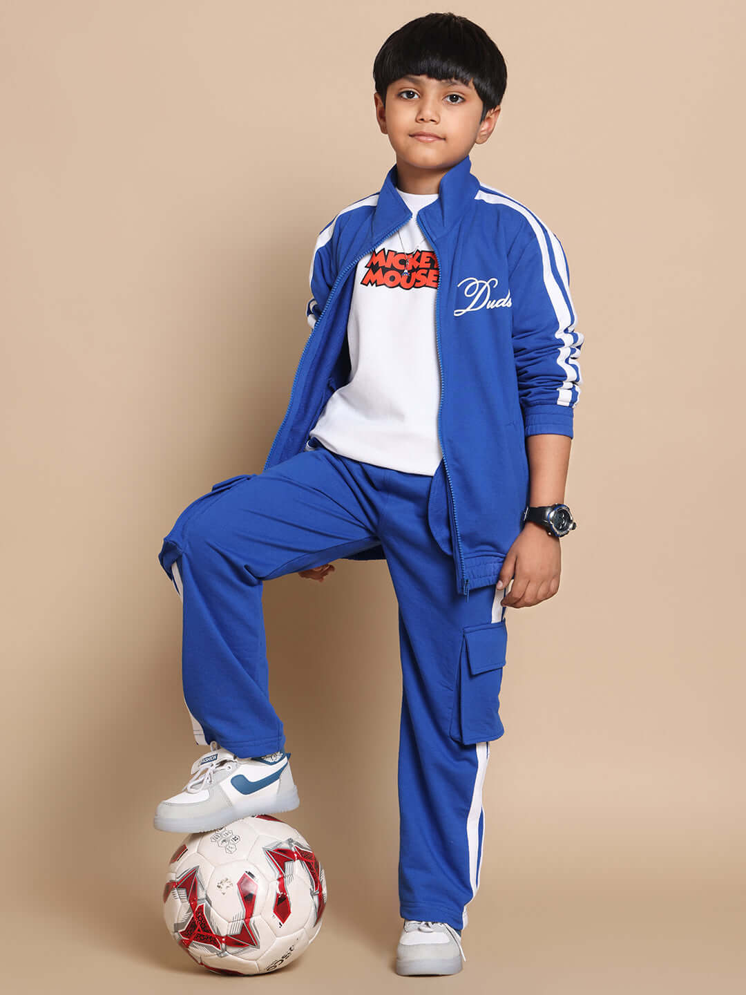 Child wearing a royal blue SCOTIA CO-ORD set, featuring a jacket and pants, designed for both boys and girls, standing with a soccer ball.