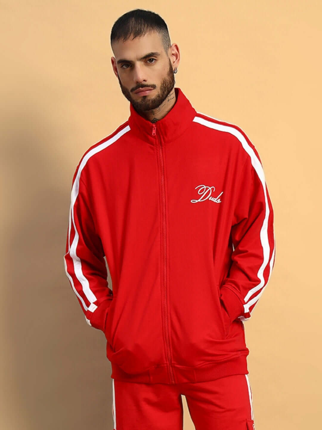 Model wearing red SCOTIA JACKET with white stripes by DUDS, hands in pockets, set against a beige background.