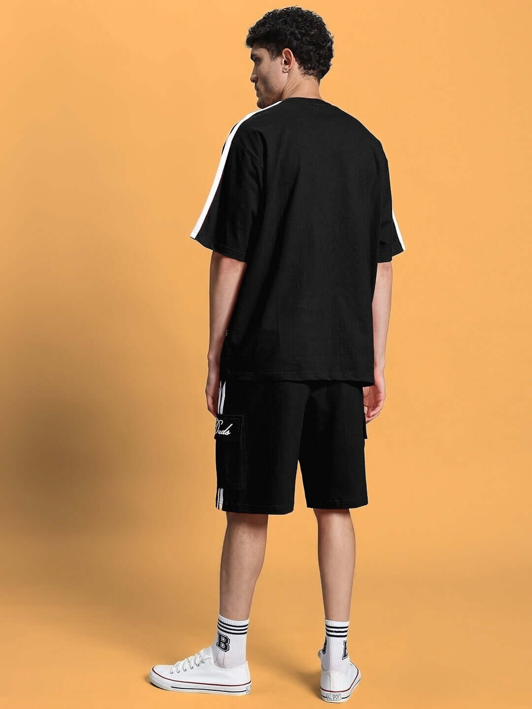Model wearing SCOTIA SUMMER CO-ORD SET BLACK against a peach background showcasing back view.