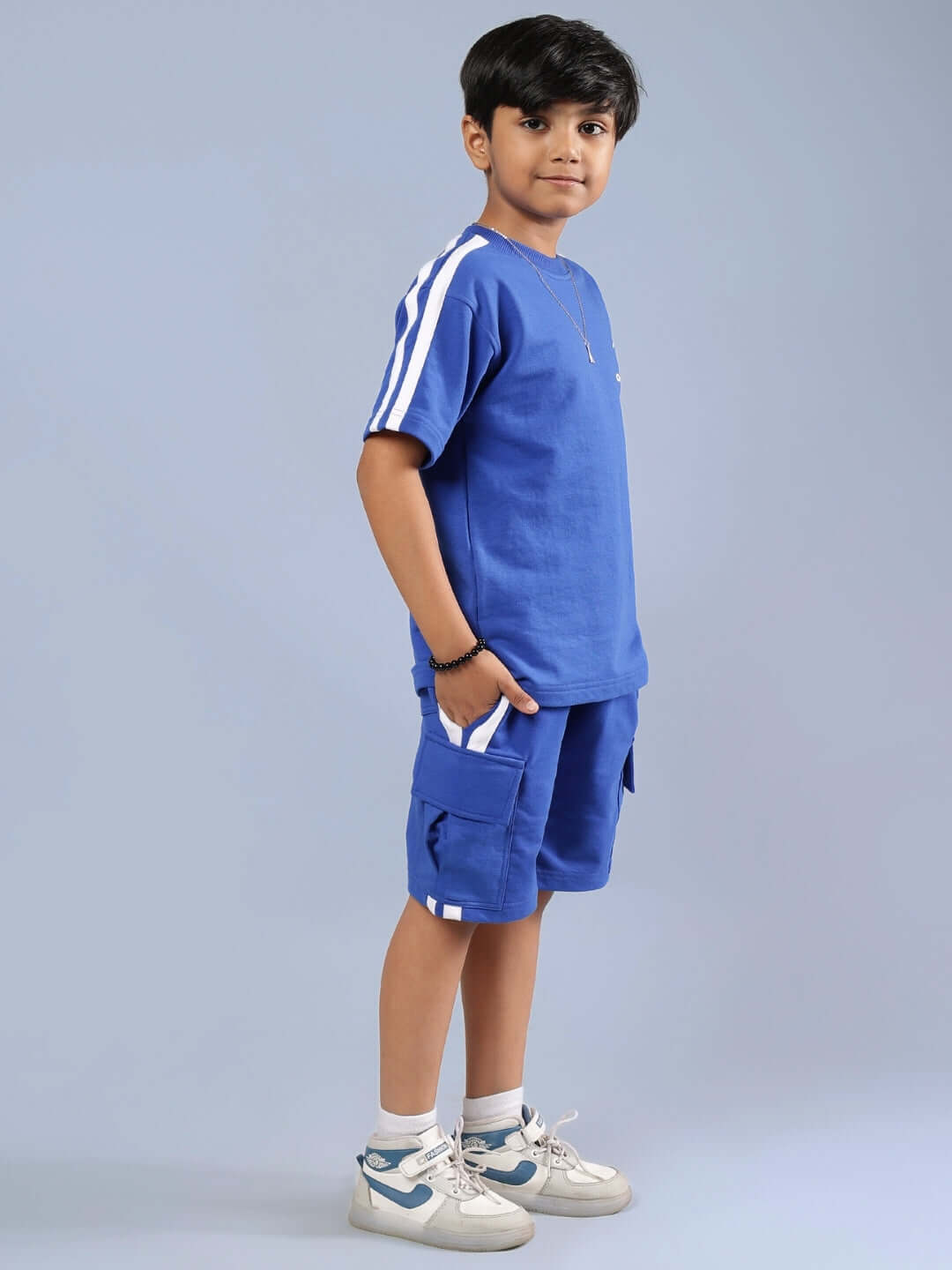 Boy wearing royal blue summer co-ord set by Scotia, featuring side stripes and pockets; perfect for boys and girls. Ideal for custom fit orders.