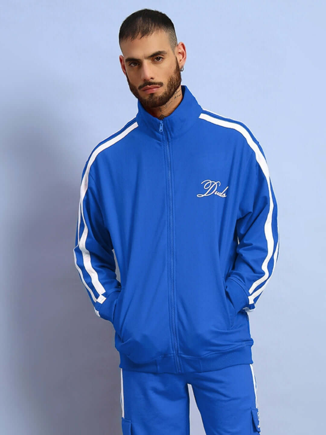 Man wearing a royal blue Scotia jacket by DUDS, featuring white stripes and logo, standing against a blue background.