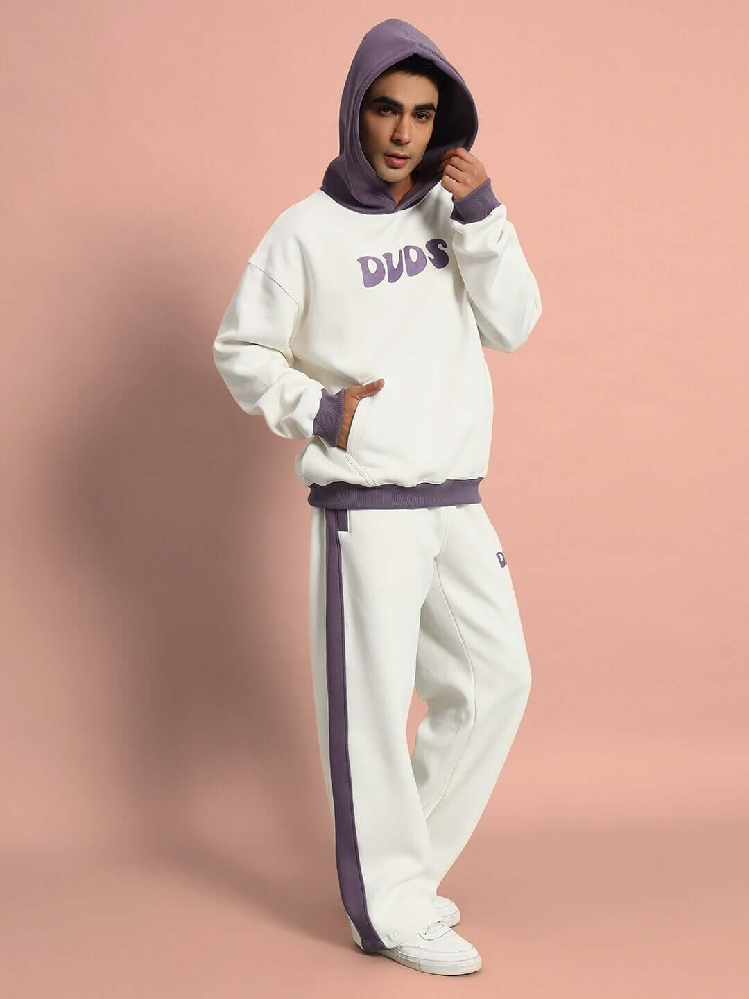 Person wearing SELF LOVE FLEECE OVERSIZED HOODIE WHITE VIOLET with matching pants, posing stylishly against a pink background.