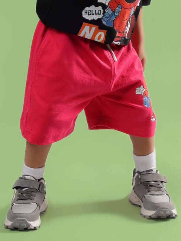 Child wearing SESAME SHORTS FOR BOYS & GIRLS PINK with sneakers, standing on green background.