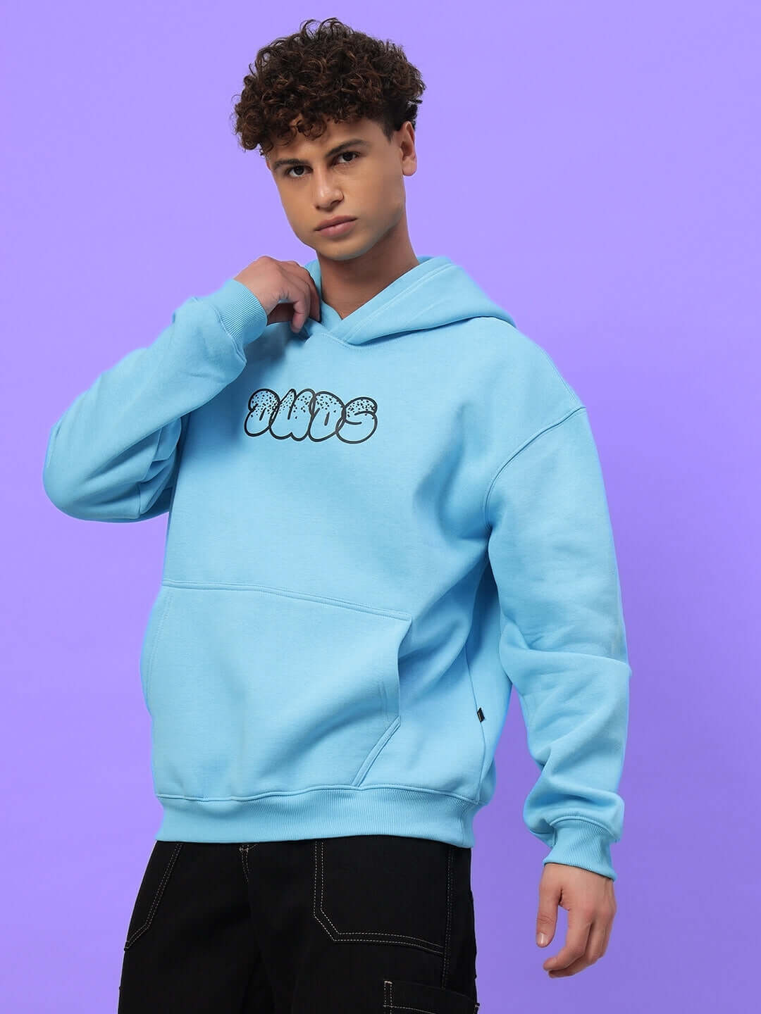Model wearing SHARKWAVE OVERSIZED FLEECE HOODIE LIGHT BLUE with graphic text, showcasing trendy streetwear style on a purple background.