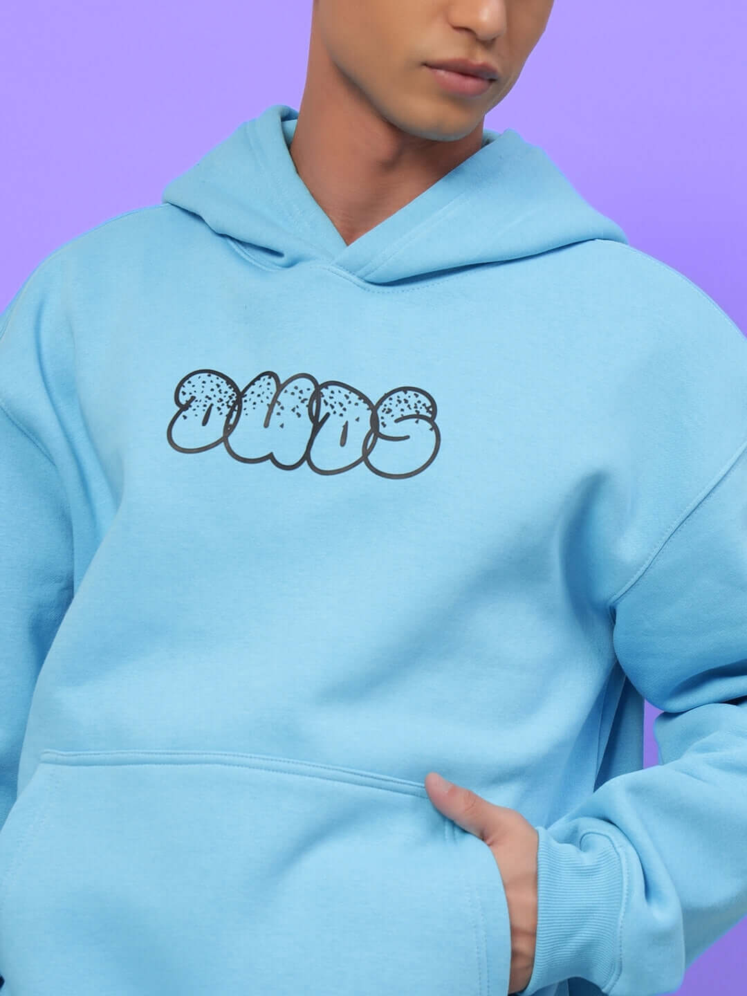 Model wearing SHARKWAVE OVERSIZED FLEECE HOODIE LIGHT BLUE with logo, showcasing relaxed fit and soft fleece material against purple background.