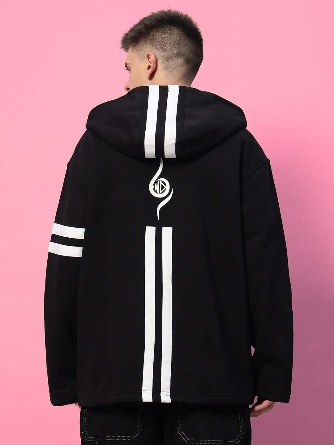 Back view of SHINOBI ZIPPER LONG LENGTH FLEECE HOODIE BLACK with white stripes, worn by a male model against a pink background.