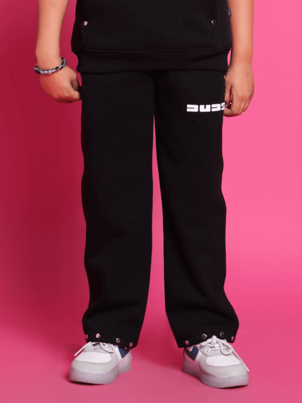 Child wearing black shooter fleece pants, stylish and comfortable for boys and girls, standing against a pink background.