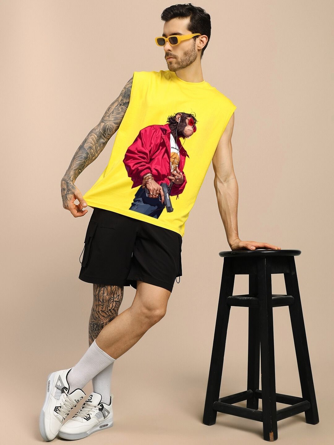 Man wearing SHOOTER MONKEY GYM T-SHIRT YELLOW with graphic print, leaning on stool.