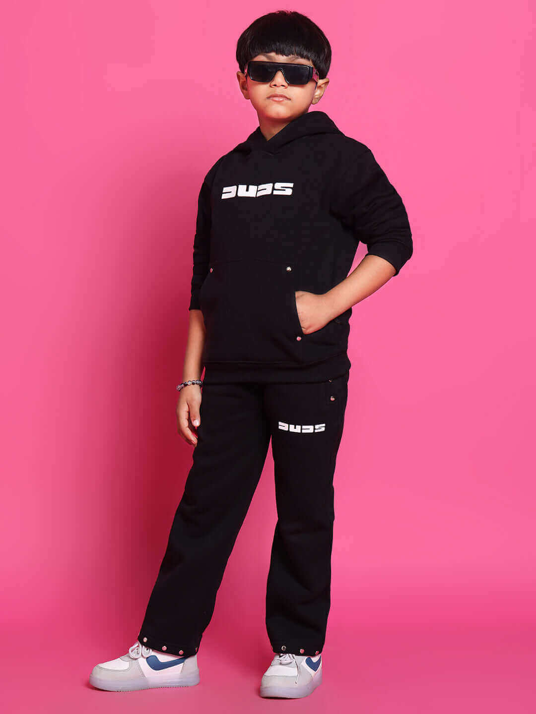 Child wearing black Shooter co-ord set with hoodie and pants from DUDS, designed for boys and girls, against pink background.