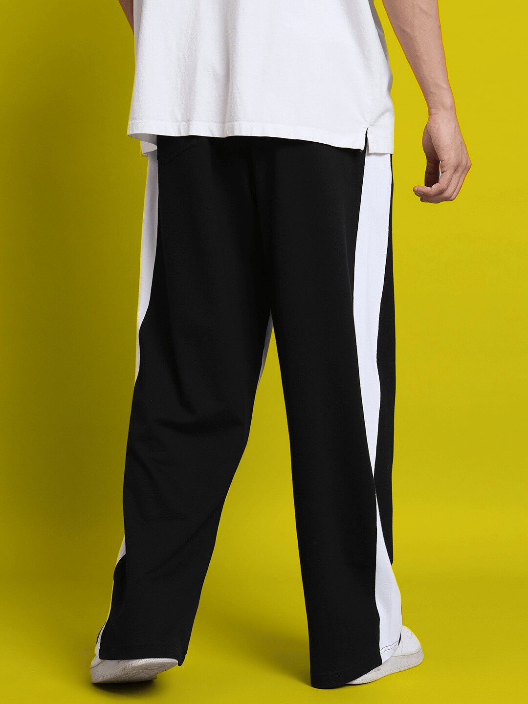 Model wearing black side seam baggy joggers with a white shirt on a yellow background.