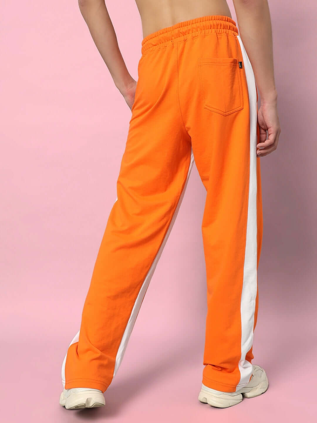 Model wearing orange side seam baggy joggers with white stripe, showcasing the back view, made to order by DUDS Tailors.