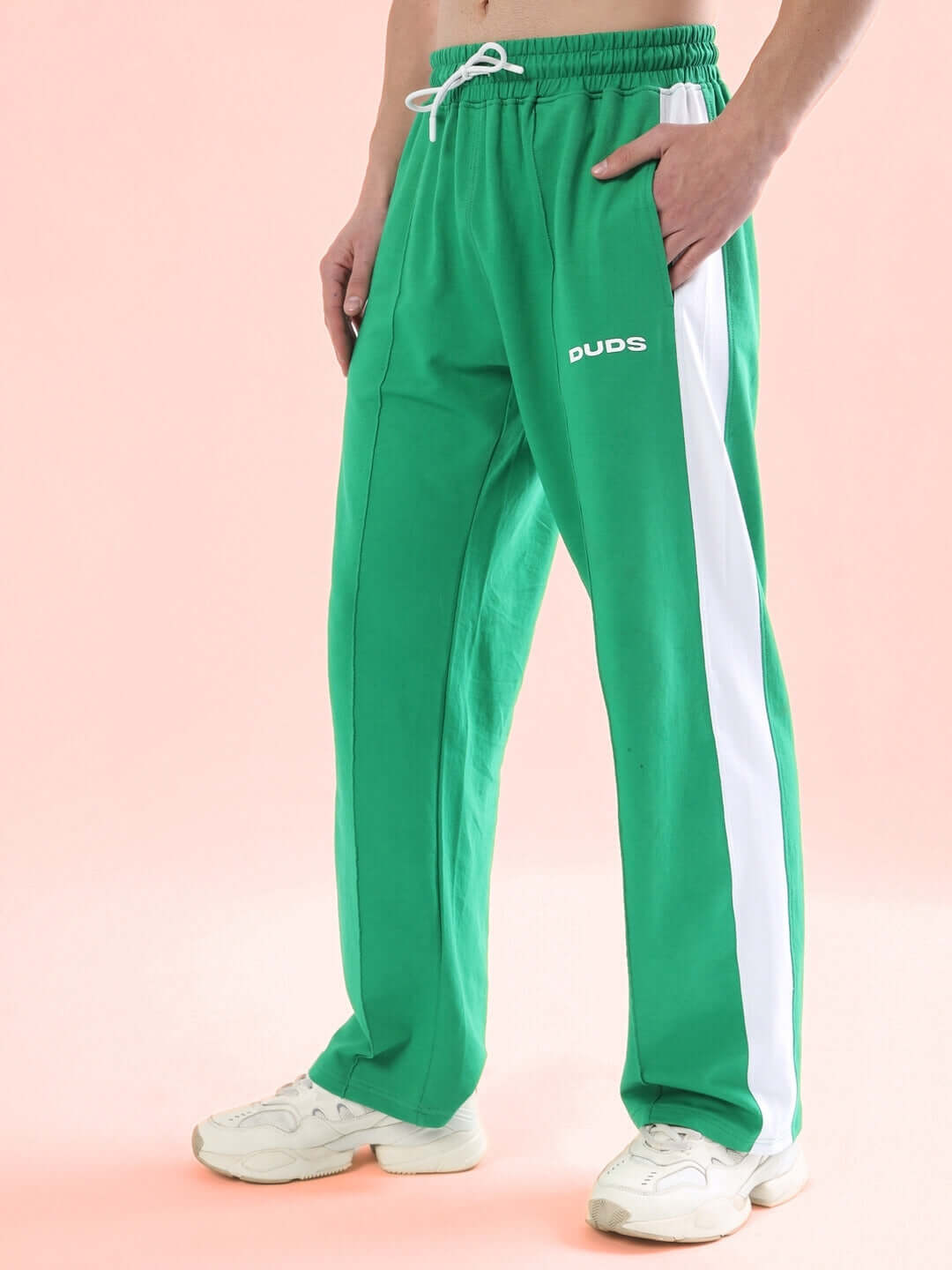 Model wearing green side seam joggers with white stripe, featuring DUDS logo, showcasing casual style and comfort on pink background.