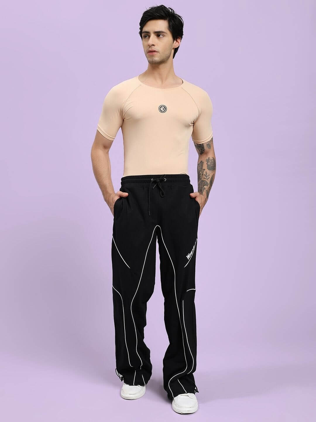 Man wearing SIGNATURE PIPING JOGGERS BLACK with contrast piping and a beige shirt against a purple background.