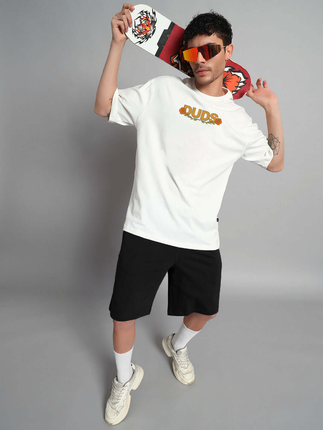 Model wearing off-white oversized T-shirt with sitting lion print, paired with black shorts and sunglasses, holding graphic scarf.