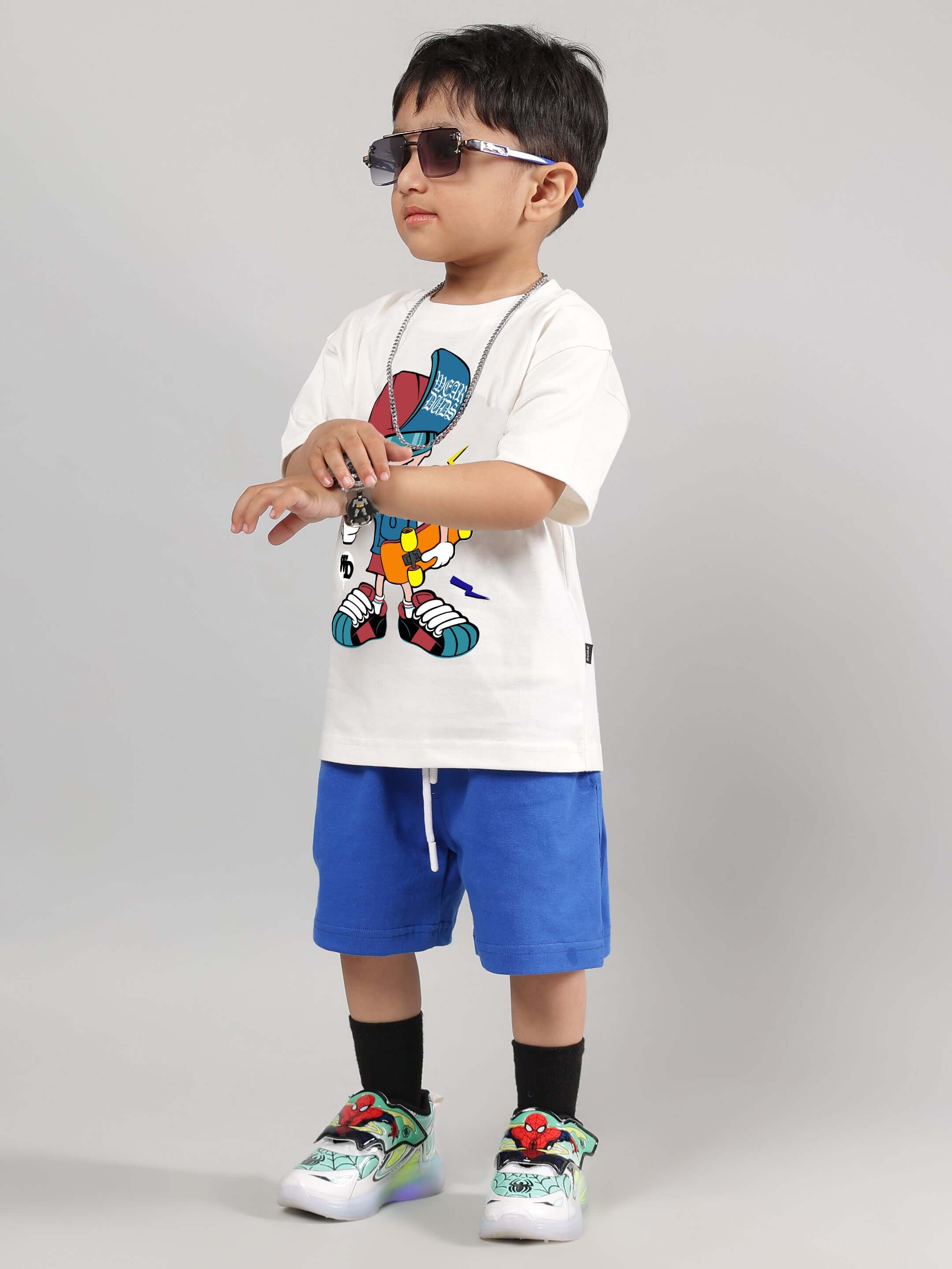 Boy wearing SKATE RIDER CO-ORD for kids in off white and royal blue, featuring trendy skateboard graphics, styled with sunglasses.