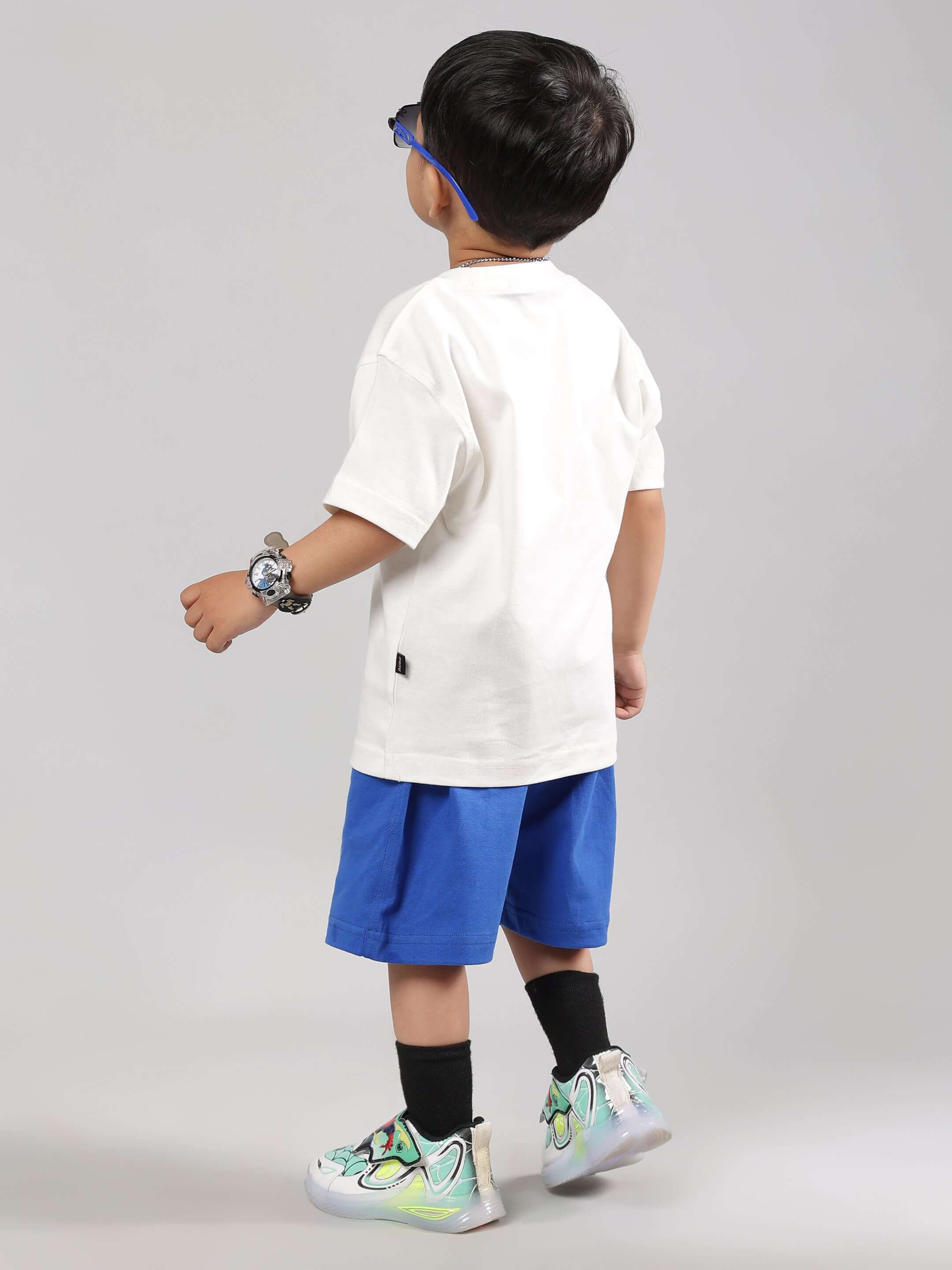 Boy wearing off-white skate rider t-shirt with blue shorts and stylish sneakers, showcasing casual outfit for kids by DUDS.