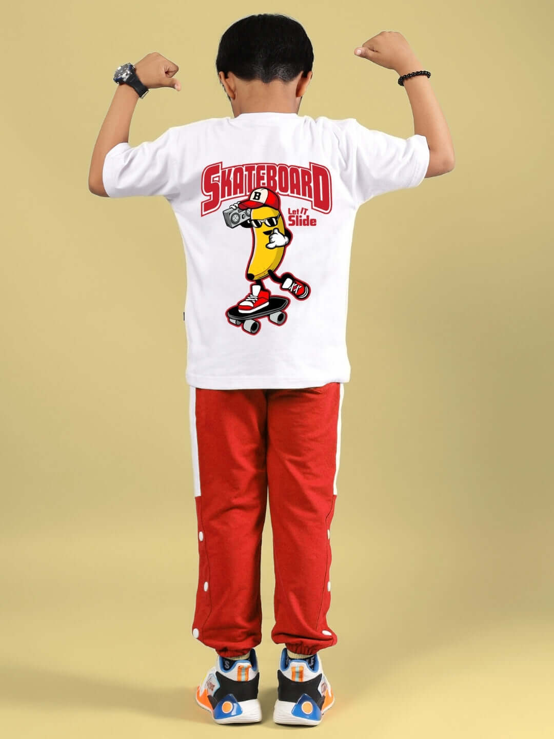 Child wearing white and red skater banana co-ord, featuring skateboard graphic, flexing arms. Ideal for boys and girls. Made to order.