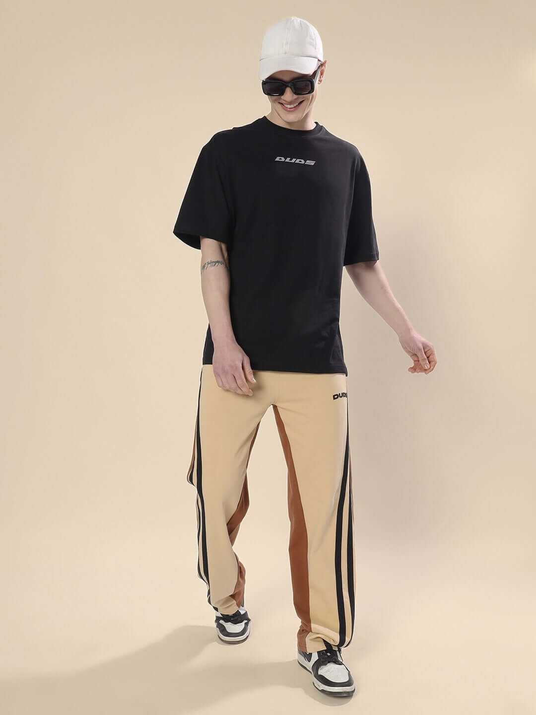 Model wearing SKATER KOREAN BAGGY JOGGERS in cream brown with black t-shirt and cap standing against beige background.
