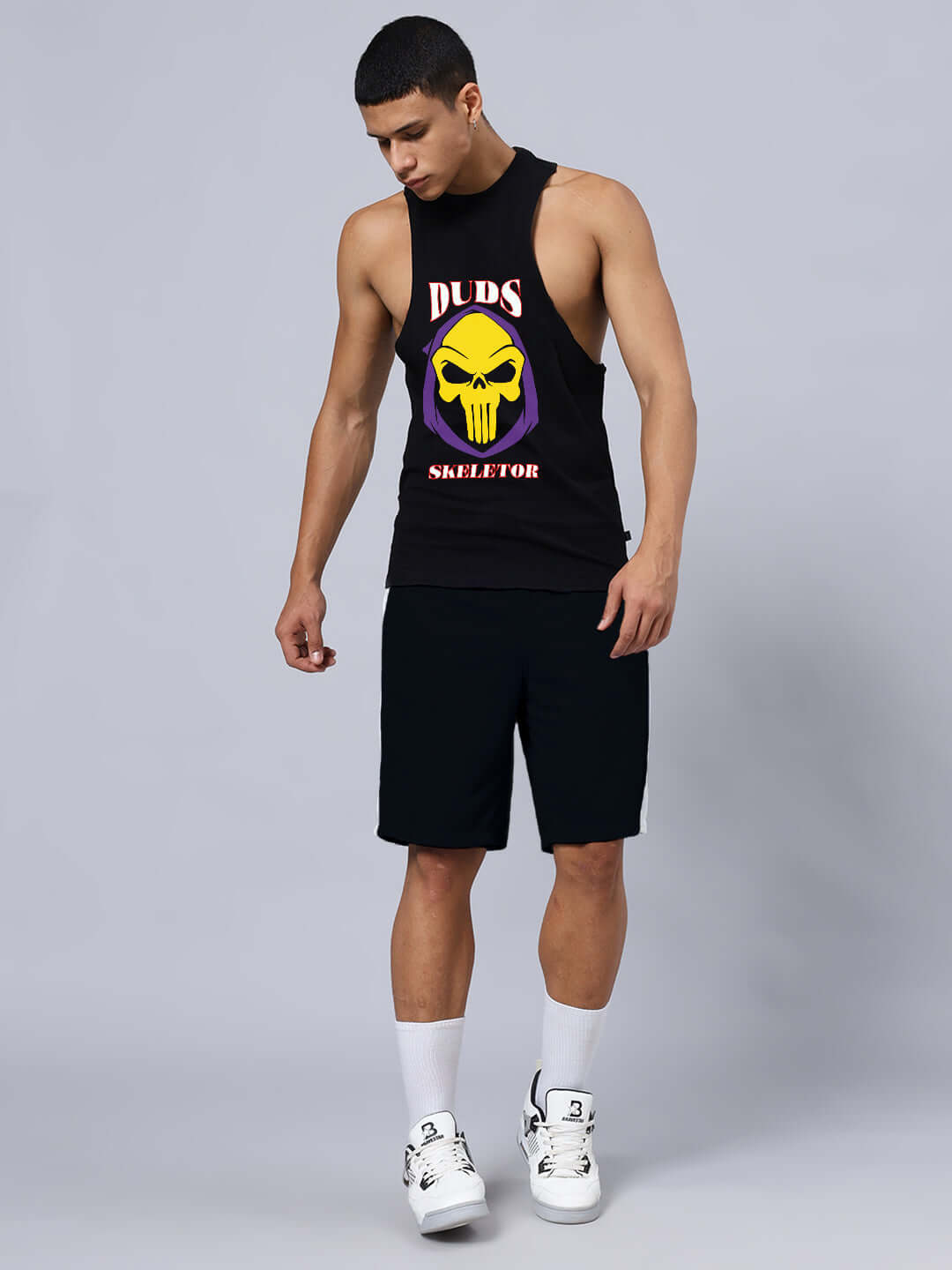 Man wearing SKELETOR GYM CO-ORD SET SELEEVELESS BLACK with printed design on front, white sneakers, showcasing gym apparel style.