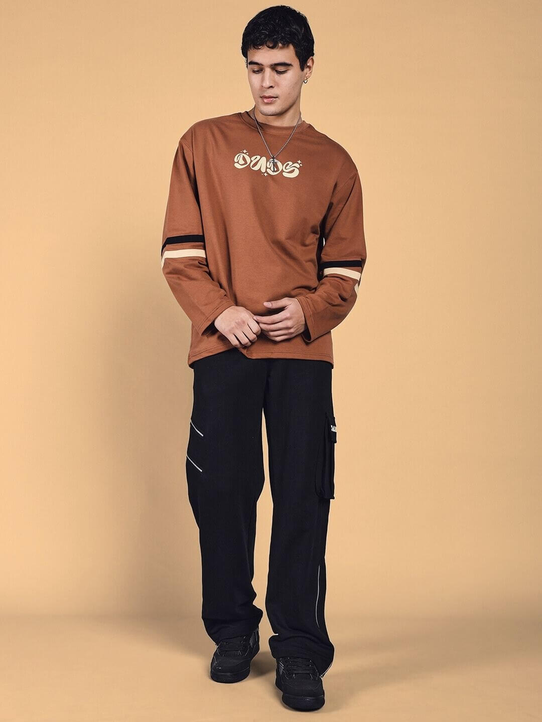 Model wearing black SKIDDER cargo pants and brown sweater, showcasing comfortable, customizable streetwear by DUDS.