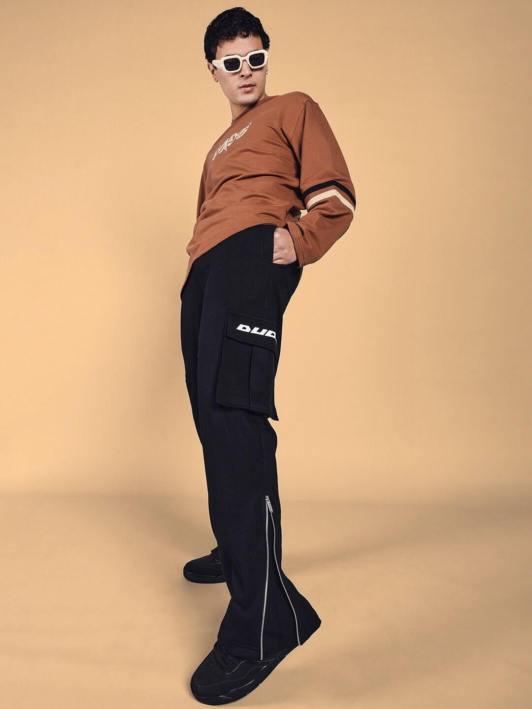 Man wearing black Skidder Cargo Pants by DUDS, standing confidently with a styled pose and sunglasses.