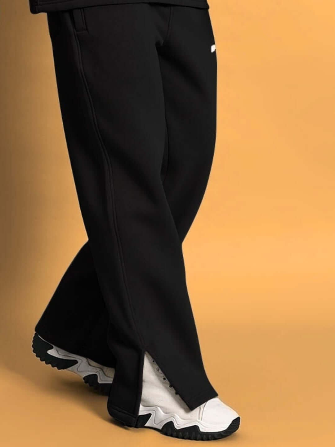 SKODA black cotton fleece jogger pants with white sneakers against a beige background.