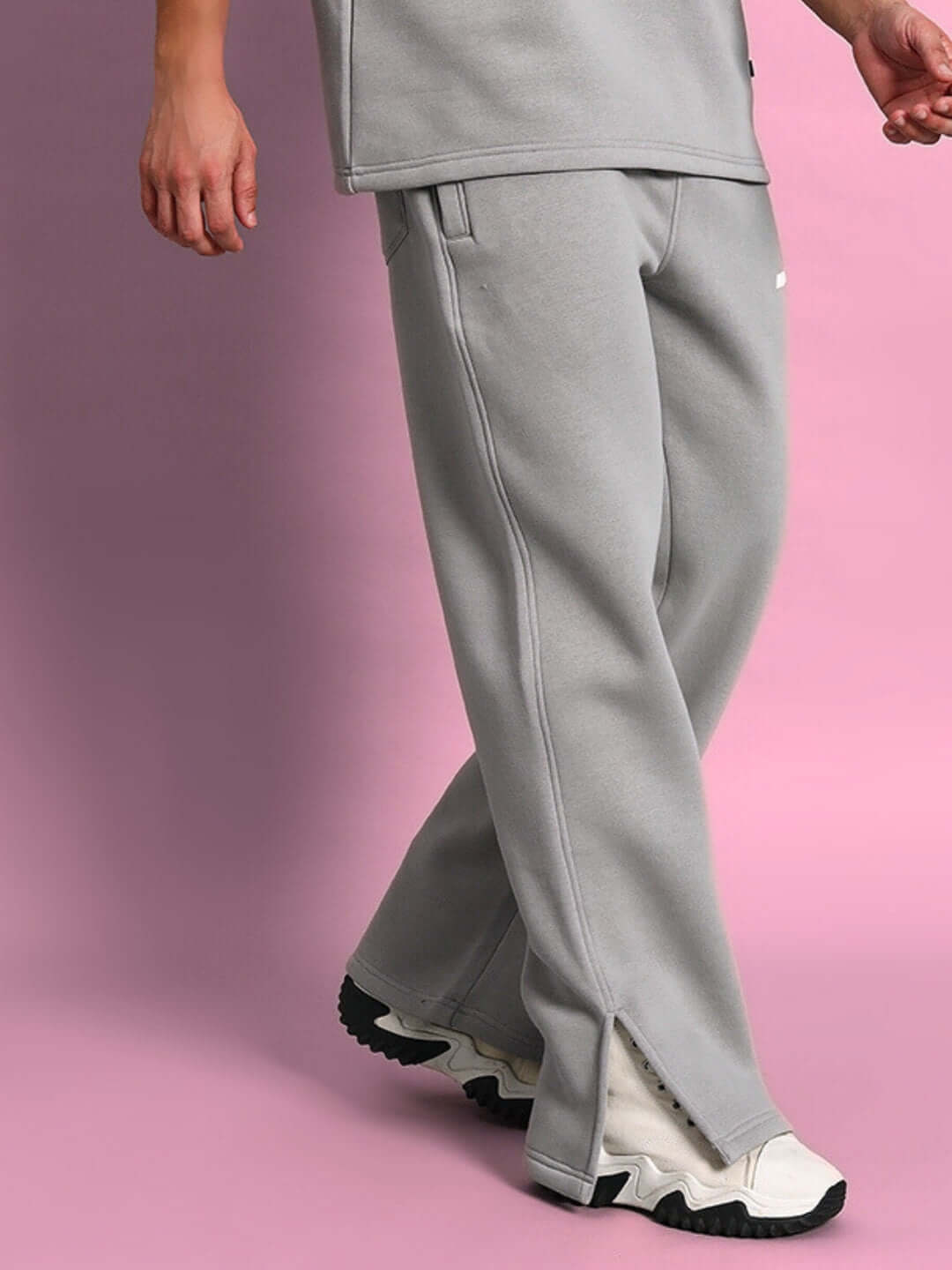 Person wearing grey SKODA cotton fleece joggers with split hem, paired with white sneakers against a pink background.