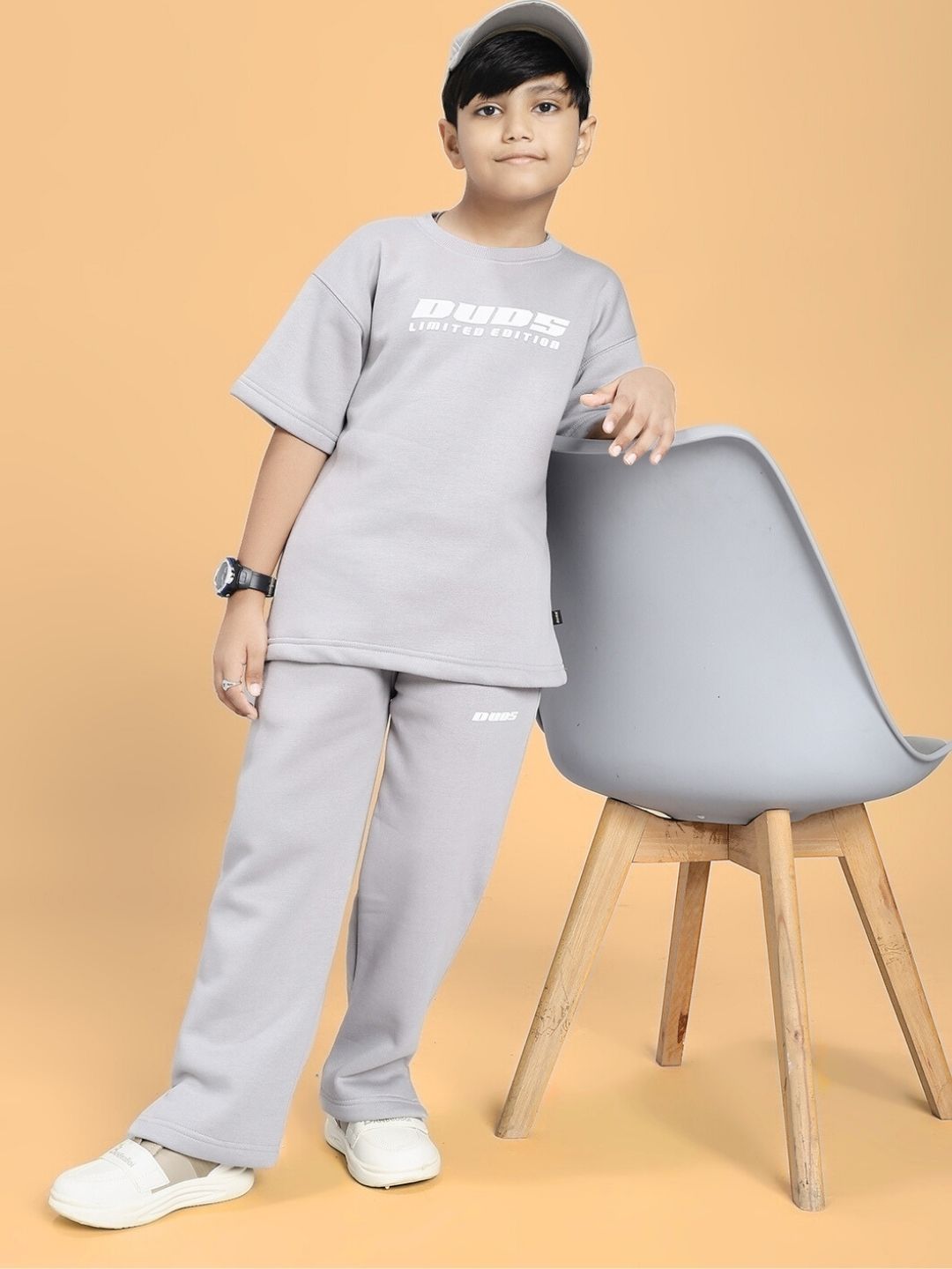 Child wearing SKODA FLEECE T-SHIRT FOR BOYS AND GIRLS GREY, standing next to a chair, showcasing the unisex skater style.
