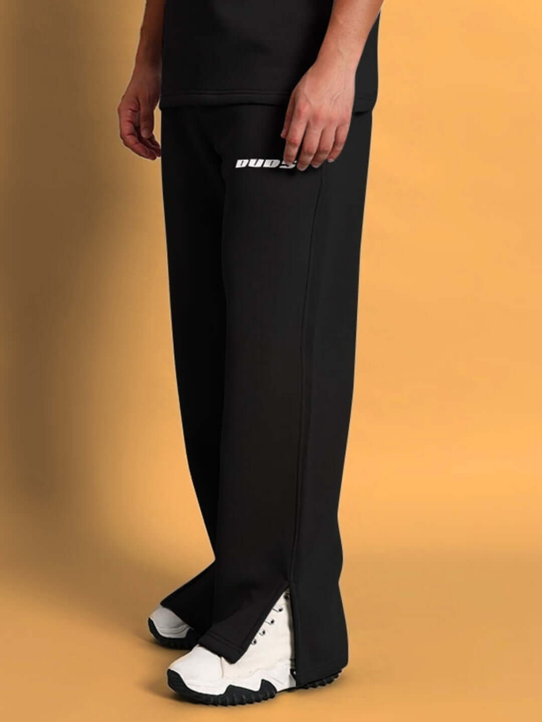 Person wearing black SKODA cotton fleece jogger with white sneakers against a tan background.