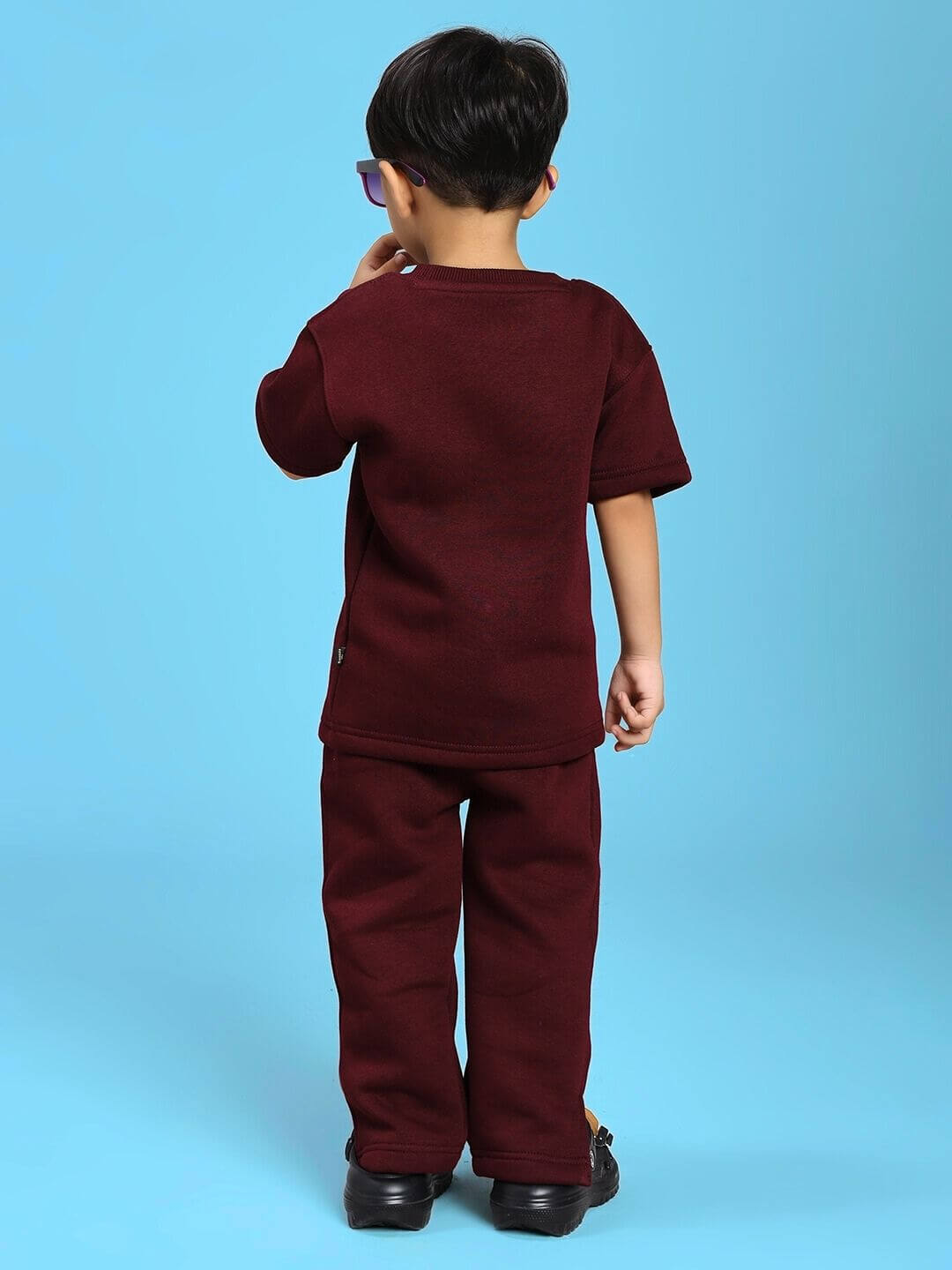 Child wearing SKODA FLEECE CO-ORD FOR BOYS AND GIRLS MAROON, back view of maroon outfit, blue background.
