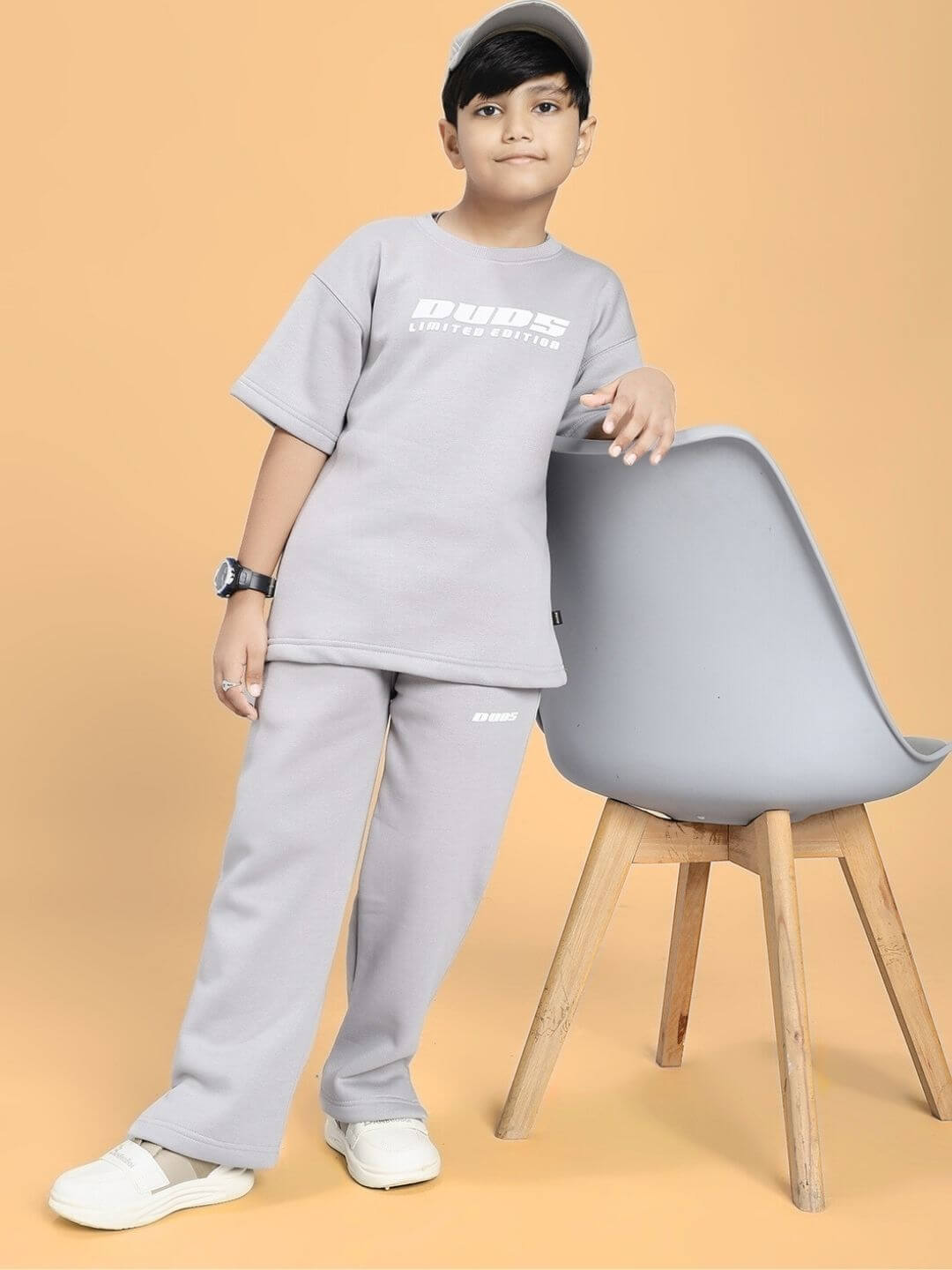 Boy wearing SKODA FLEECE CO-ORD FOR BOYS AND GIRLS GREY next to a chair, showcasing cozy and trend-forward design in a studio setting.