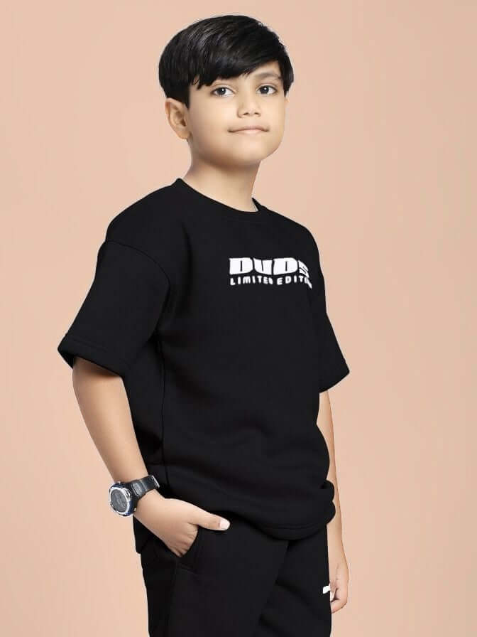 Young boy wearing SKODA FLEECE T-SHIRT FOR BOYS AND GIRLS BLACK with stylish watch, standing against a peach background.