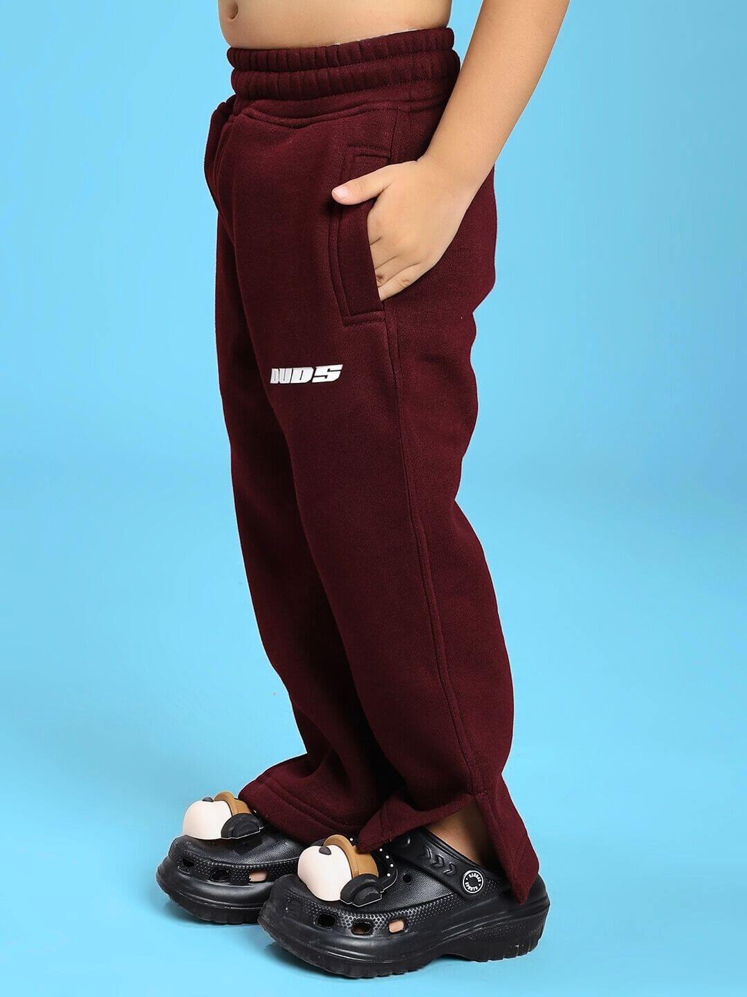 Child wearing SKODA FLEECE CO-ORD FOR BOYS AND GIRLS MAROON pants with crocs on a blue background.