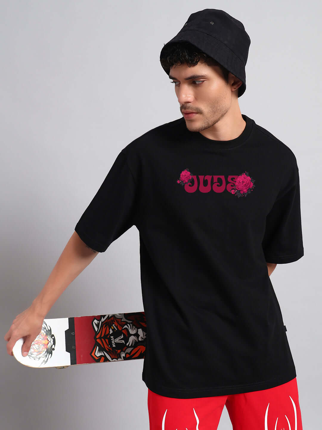 Man wearing SKULL ROSES OVERSIZED T-SHIRT BLACK, holding a skateboard, in a casual street style look.