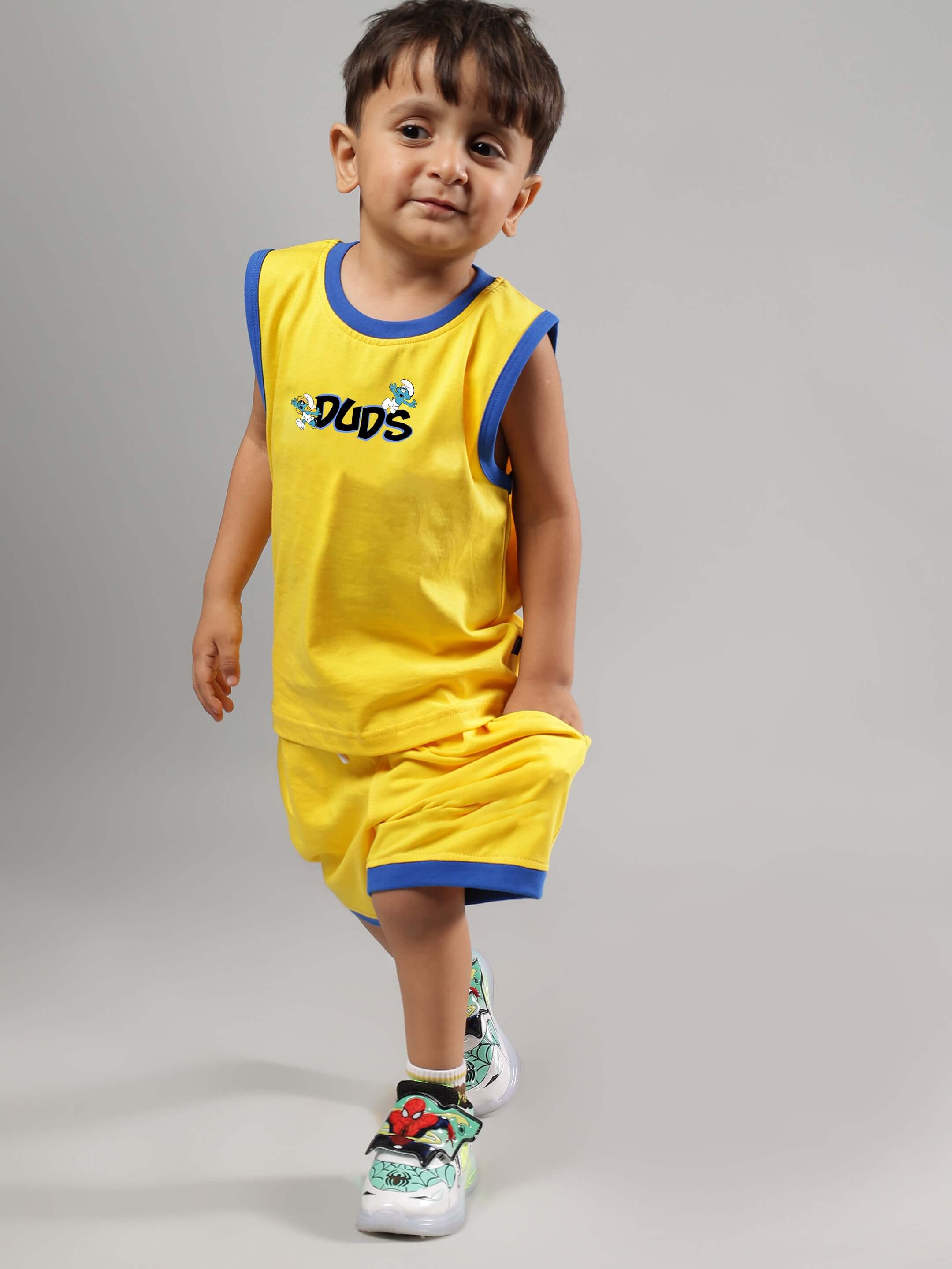 Child wearing a yellow SMURFS HOME T-shirt and shorts set, smiling, with colorful sneakers. Perfect for boys and girls.