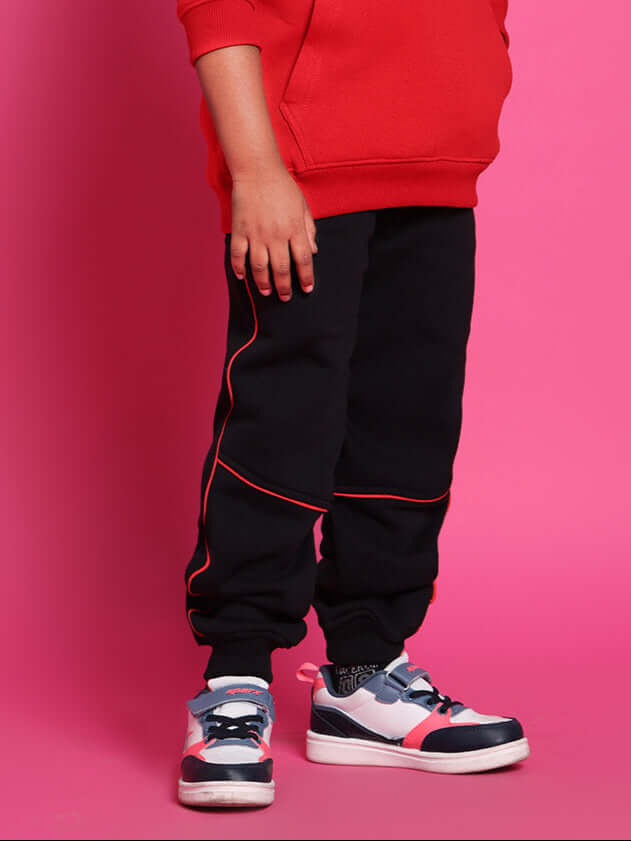 Child wearing Snail relaxed fit jogger pants in black, suitable for boys and girls, with colorful sneakers, standing against a pink background.