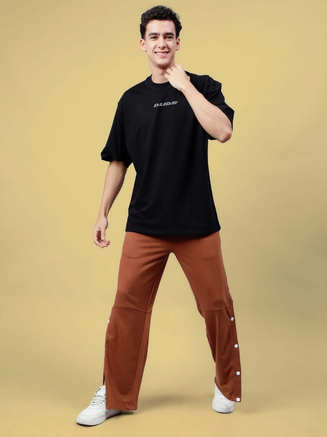 Model wearing Sonic Sound Reflector Oversized Black T-Shirt, premium cotton fabric, styled with brown pants, on beige background.